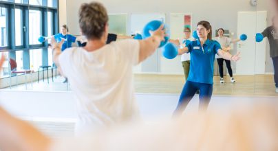 Therapeutin leitet Bewegungsgruppe mit Gymnastikbällen an, aktive Therapie, Gruppenübung, Balance Aschaffenburg